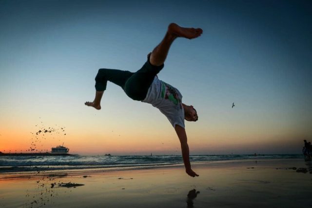 young man flipping on a beach at sunset